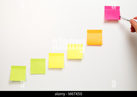 A male hand writing with marker on top blank sticky notes ascendant line attached on white background Stock Photo