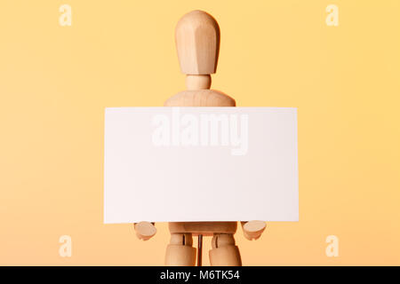 Artistic wooden mannequin doll holding blank business card on orange background Stock Photo