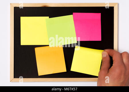 A male hand hanging different colours blank sticky notes on blackboard against white background Stock Photo