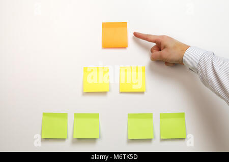 A male hand pointing on top of blank multicolored sticky notes pyramid attached on white background Stock Photo