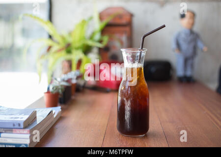 Cold black coffee with ice in bottle on wood table in coffee shop Stock Photo