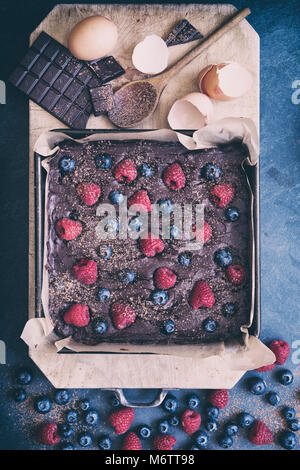 Homemade raw chocolate raspberry and blueberry brownie mixture in a baking tray with ingredients on a slate background Stock Photo