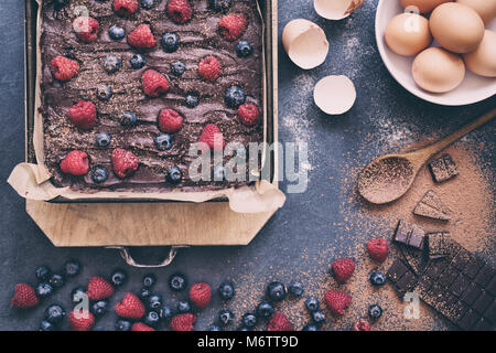 Homemade raw chocolate raspberry and blueberry brownie mixture in a baking tray with ingredients on a slate background Stock Photo