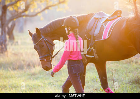 Young rider girl walking with horse in park. Equestrian recreation activities background with copy space Stock Photo