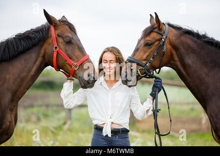 Young rider girl having fun with two her horses. Equestrian sport concept background Stock Photo