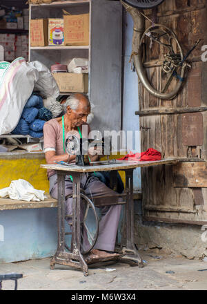 Portrait of an elderly Indian man using a treadle (pedal) sewing machine outside his house in Samode Village, Rajasthan, India Stock Photo