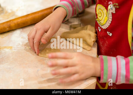 Little girl rolls out the dough. The child makes pastry with dough from forms. Stock Photo