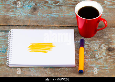 Open notebook with handwritten drawn yellow highlighter stripes and cup of coffee on wooden desk. Stock Photo