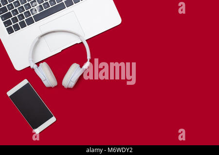 Office desk table with laptop, smartphone, and headphones. Flat lay with copy space on red background Stock Photo