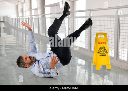 Hispanic businessman falling on wet floor inside office building Stock Photo
