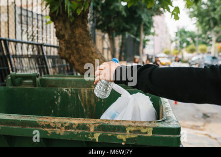 A man in the street throws a plastic bottle into a container with waste. Care for the environment. Eco friendly. Stock Photo