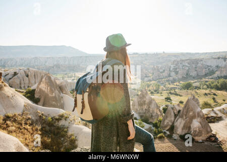 A traveler in a hat with a backpack stands on a mountain and looks at a beautiful view in Cappadocia in Turkey. Journey. Hiking. Stock Photo