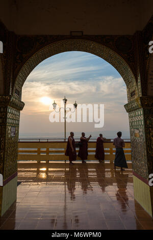 Three monks and an other man the ornate Sutaungpyei Pagoda at the Mandalay Hill in Mandalay,  Myanmar (Burma) at sunset. Stock Photo