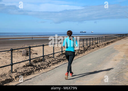 Woman running on the seafront promenade at Crosby, Merseyside.  UK Weather. 7th March, 2018.  Sunny start to the day on Mariners Way as people take light exercise on the promenade seafront. Credit: MediaWorldImages/AlamyLiveNews. Stock Photo