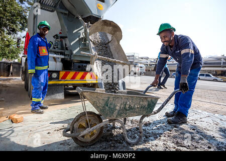 Cement mixer pouring cement into wheelbarrow.  Johannesburg, South Africa. Stock Photo