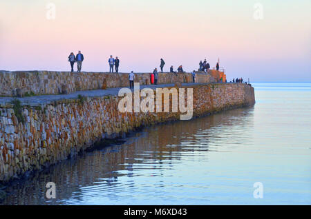 people walk along the harbour pier wall at St andrews, Fife, Scotland on a calm clear summer evening Stock Photo