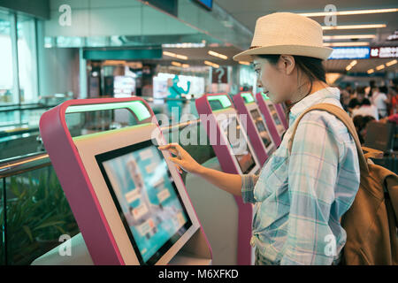 Young Asian woman at self service transfer area doing self check in at automated machine with touch screen display in the international airport termin Stock Photo