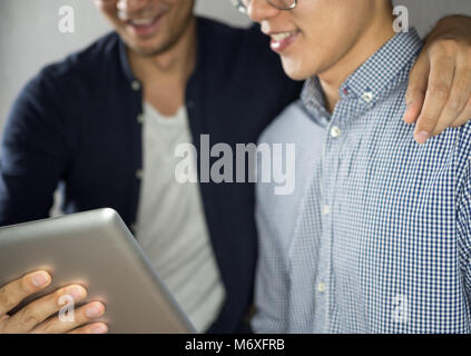 Men using tablet hugging and talk looking happy Stock Photo