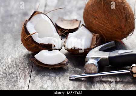 cracked  coconuts and hammer on old wooden table Stock Photo