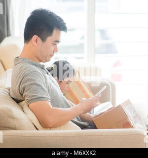 Man scanning QR code with smart phone. Asian family at home, living lifestyle indoors. Stock Photo