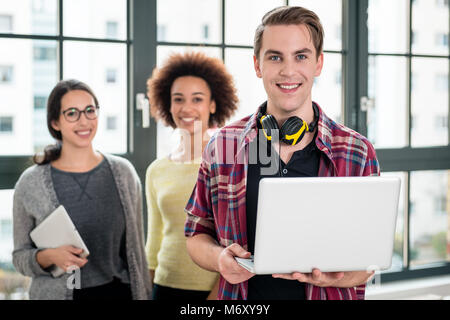 Portrait of young man smiling while holding a laptop at work Stock Photo