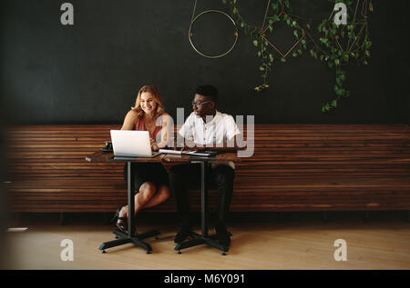 Business partners at a coffee shop working on a laptop computer. Friends sitting at a coffee table with laptop and notepads doing work. Stock Photo