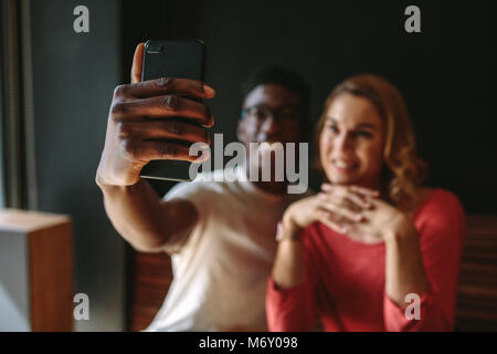 Smiling couple taking a selfie using mobile phone. Man and woman sharing happy moments at a coffee shop. Stock Photo