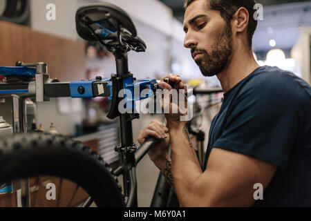 Worker repairing a bicycle at workshop. Man fixing a bicycle to a holding stand in a repair shop. Stock Photo
