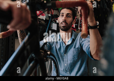 Man inspecting a bicycle handle for alignment. Mechanic working on fixing a bicycle in workshop. Stock Photo