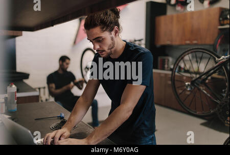 Man using laptop inside a bicycle repair workshop. Worker working on laptop while repairing a bicycle. Stock Photo