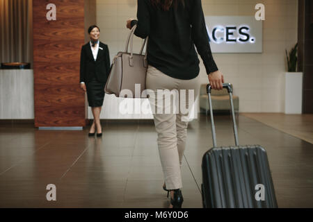Female with luggage arriving at hotel with receptionist waiting for welcoming. Business woman checking in hotel for conference. Stock Photo