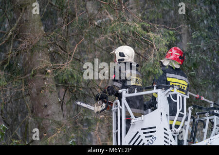 Karpacz, Poland -  February 2018 : Firefighters on the extendable crane  cutting branches of a tree for safety reasons after heavy snowfall Stock Photo