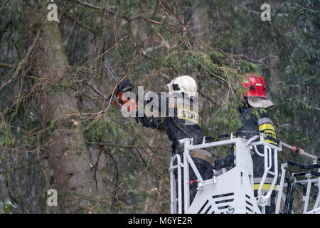 Karpacz, Poland -  February 2018 : Firefighters on the extendable crane  cutting branches of a tree for safety reasons after heavy snowfall Stock Photo