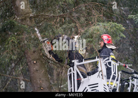 Karpacz, Poland -  February 2018 : Firefighters on the extendable crane  cutting branches of a tree for safety reasons after heavy snowfall Stock Photo