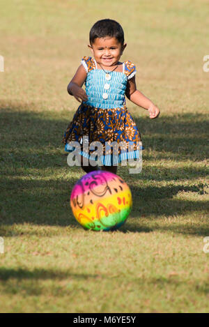 Vertical portrait of a little girl kicking a football in Viharamahadevi Park, formerly known as Victoria Park in Colombo, Sri Lanka. Stock Photo