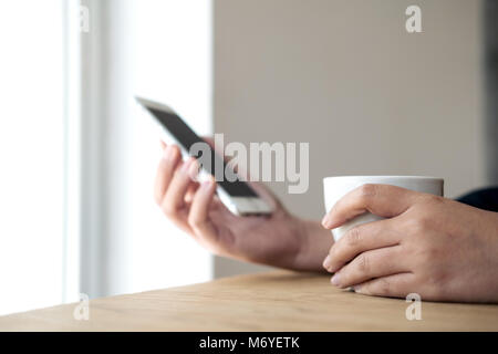 Closeup blur image of hands holding white mobile phone and coffee cup on wooden table Stock Photo