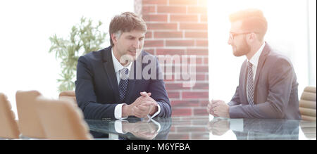 Two businessmen discussing tasks sitting at office table. Stock Photo