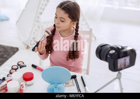 Pre-teen girl blowing on makeup brush while filming blog Stock Photo