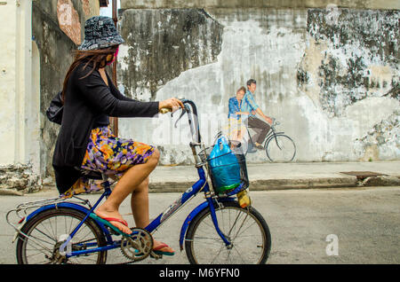 Girl on bike cycling past Penang street art Stock Photo