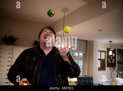 A man juggling in his house with three balls and looking up Stock Photo