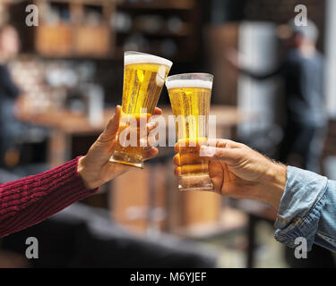 Beer glasses raised in a toast. Close-up hands with glasses. Blurred bar interior at the background. Stock Photo