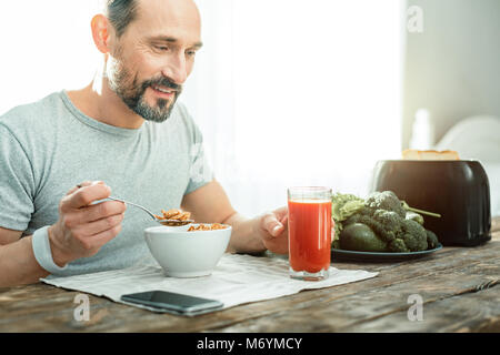 Funny joyful man eating flakes taking a glass of juice. Stock Photo