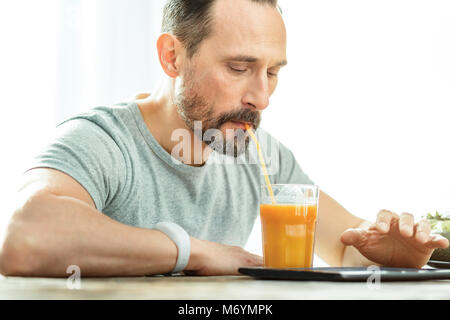 Calm occupied man drinking juice and using the tablet. Stock Photo