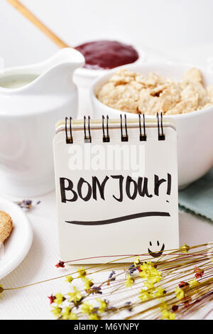closeup of a table set for breakfast with a porcelain bowl with cereals, some toasts, a bowl with jam and a note with the text bon jour, good morning  Stock Photo