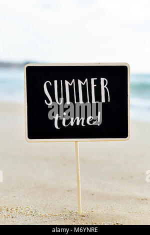 closeup of a black signboard with the text summer time written in it, on the sand of a quiet beach Stock Photo