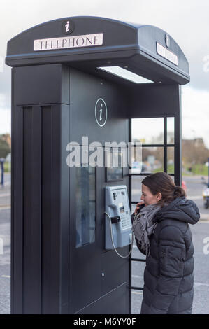 Modern telephone box in black, woman talking on a pay phone. Stock Photo