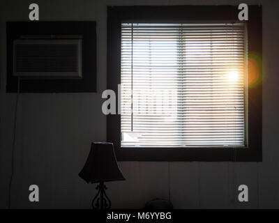 The sun is shining through closed Persian blinds of a window into a barely furnished dimmed room. Stock Photo