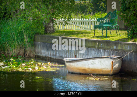 A rowing boat moored up by a coutry garden in the summer Stock Photo