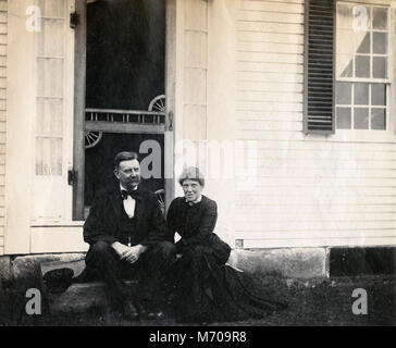 Antique circa 1905 photograph, elderly couple sitting on front step of house. Location is in or near Riggsville (now Robinhood), Maine in Sagadahoc County, USA. Stock Photo