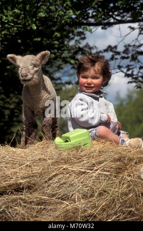 little girl and lamb sitting on hay bale Stock Photo